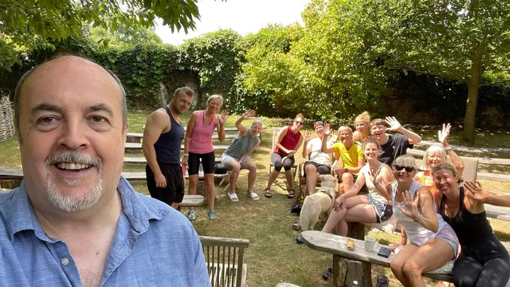 Robert and a cheerful retreat group waving from log benches in a walled garden