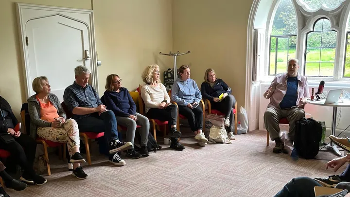 Robert teaching a seated group in a room with arched windows at St Benedict's